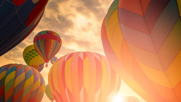 close up of six brightly coloured, mainly faded pink and orange hot air balloons at sunset