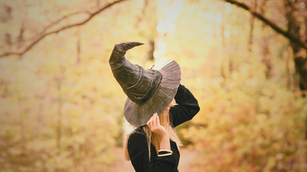 Woman in a witches hat turned side on to camera. An autumnal forest in the background.