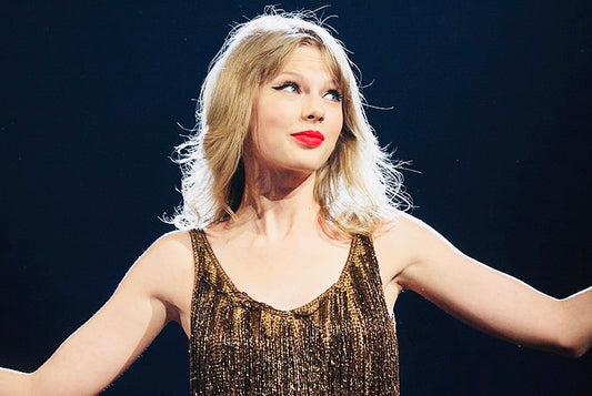 Taylor Swift on stage in gold dress, arms outstretched. 