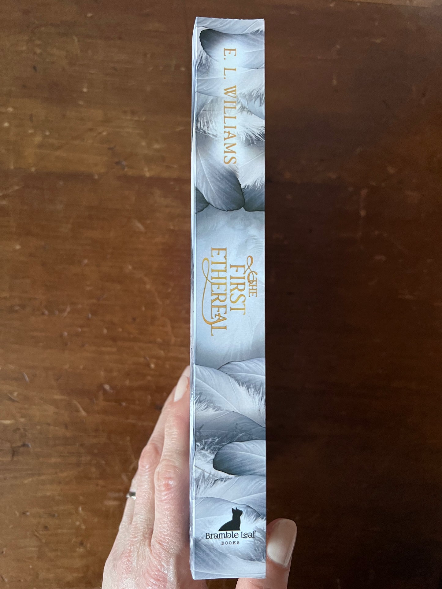 Book titled 'First Ethereal' by E.L. Williams held against a wooden background