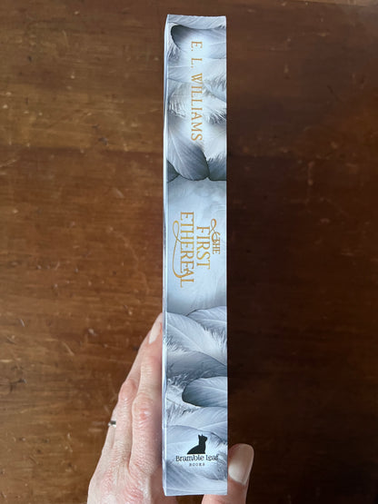 Book titled 'First Ethereal' by E.L. Williams held against a wooden background